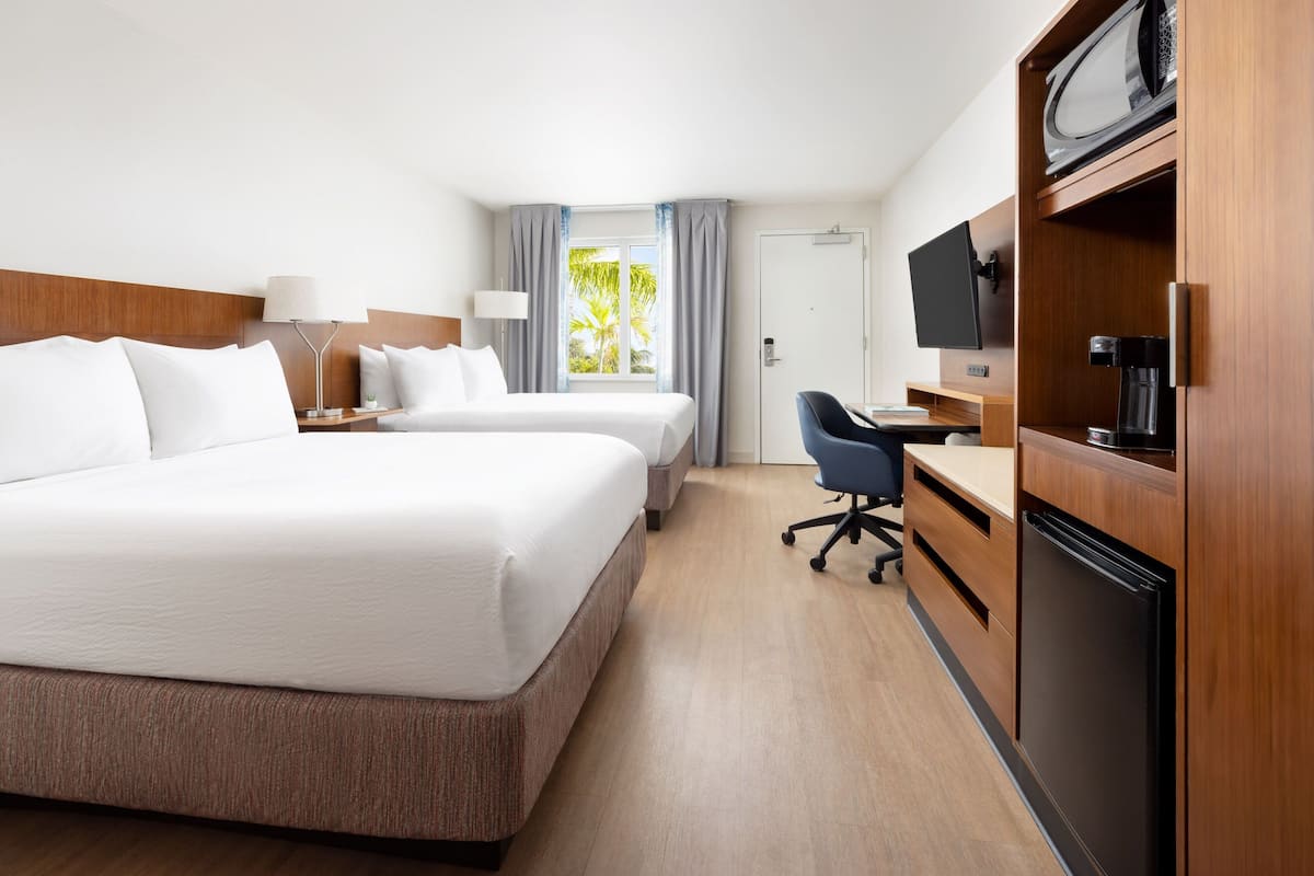 A hotel room with two beds, a desk, a chair, a television, and a refrigerator.
