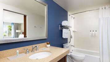 A modern bathroom with a large mirror, a sink with two faucets, a toilet, and a bathtub with a shower curtain.
