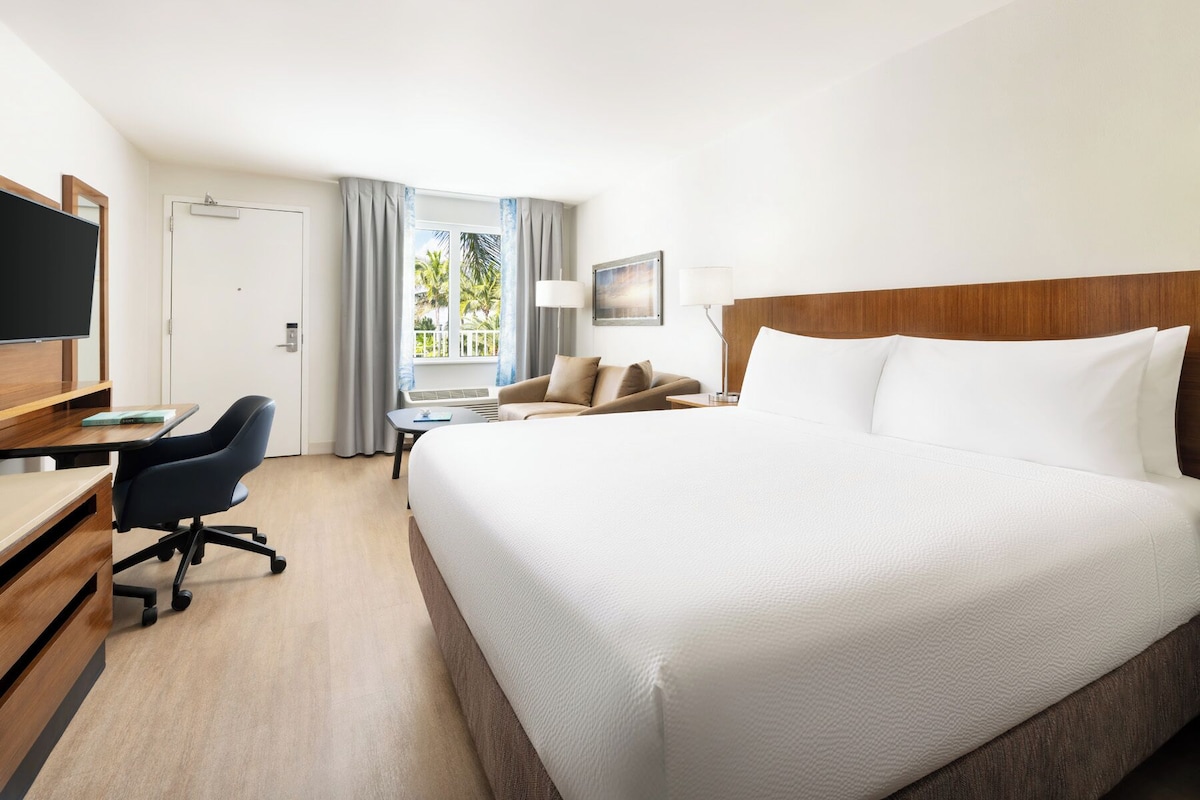 A hotel room with a large bed, a desk with a chair, a sofa, a TV, and a window with curtains.