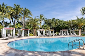 Un espace piscine agrémenté de chaises longues et de parasols, entouré de palmiers.