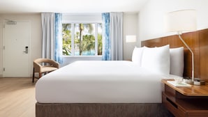 Een hotelkamer met een groot bed, een houten nachtkastje, een bureau, een stoel en een raam met gordijnen.