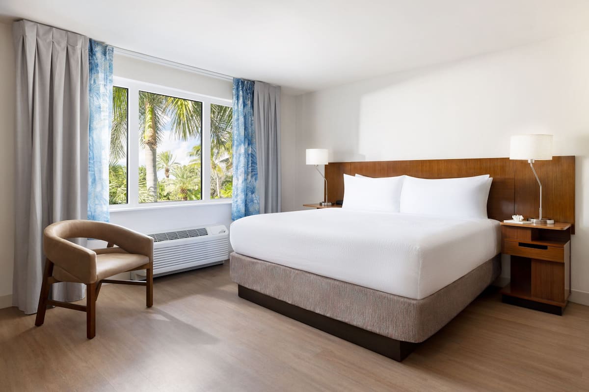 A hotel room with a large bed, a chair, a nightstand, and a window with curtains.