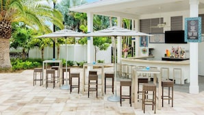 Een buitenpatio met tafels en stoelen, een bar met een counter en krukken, en een televisie aan de muur.
