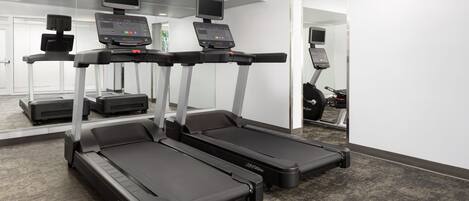 A fitness area with treadmills, a mirrored wall, and a carpeted floor.