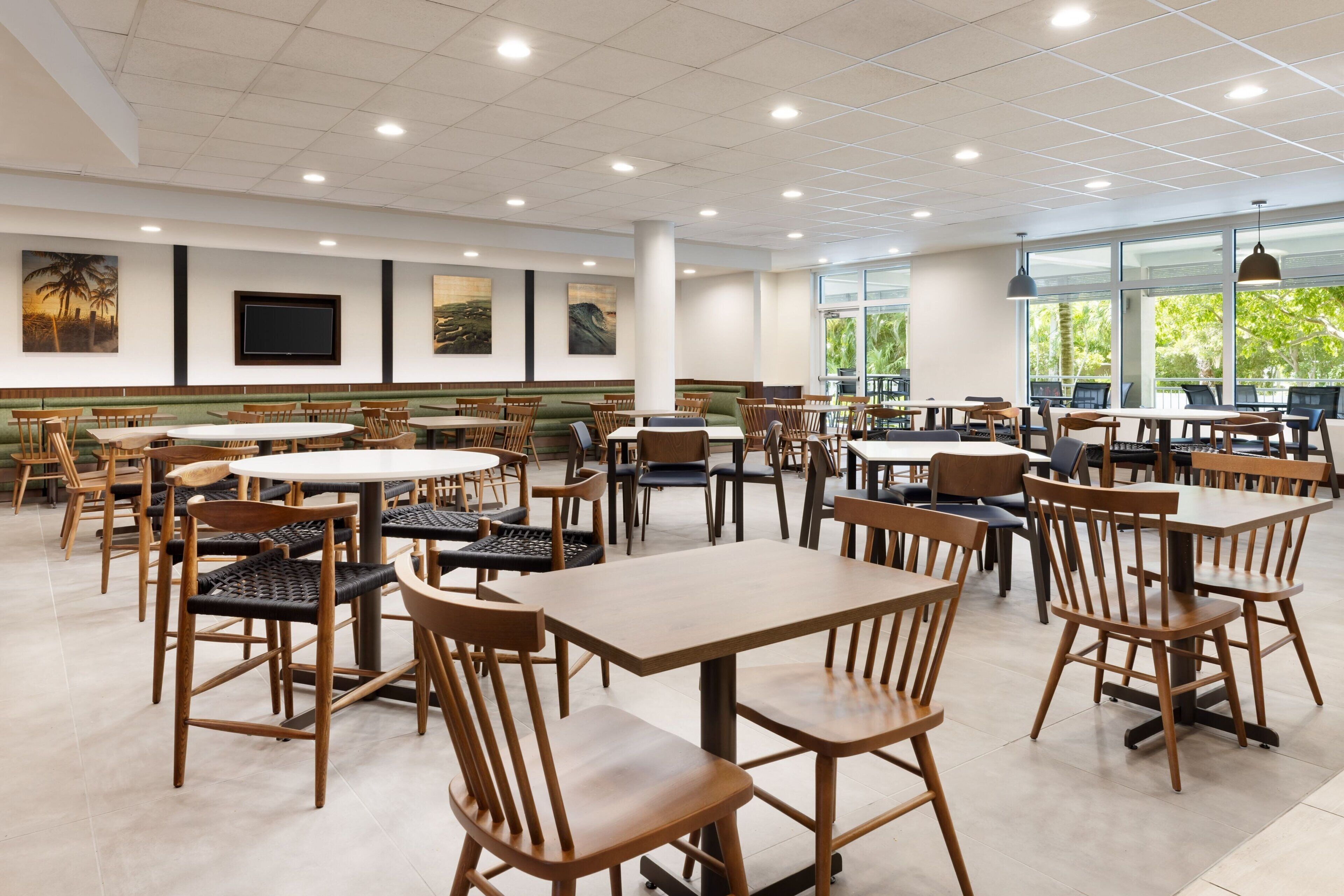 A spacious dining area with multiple tables and chairs, large windows, and artwork on the walls.