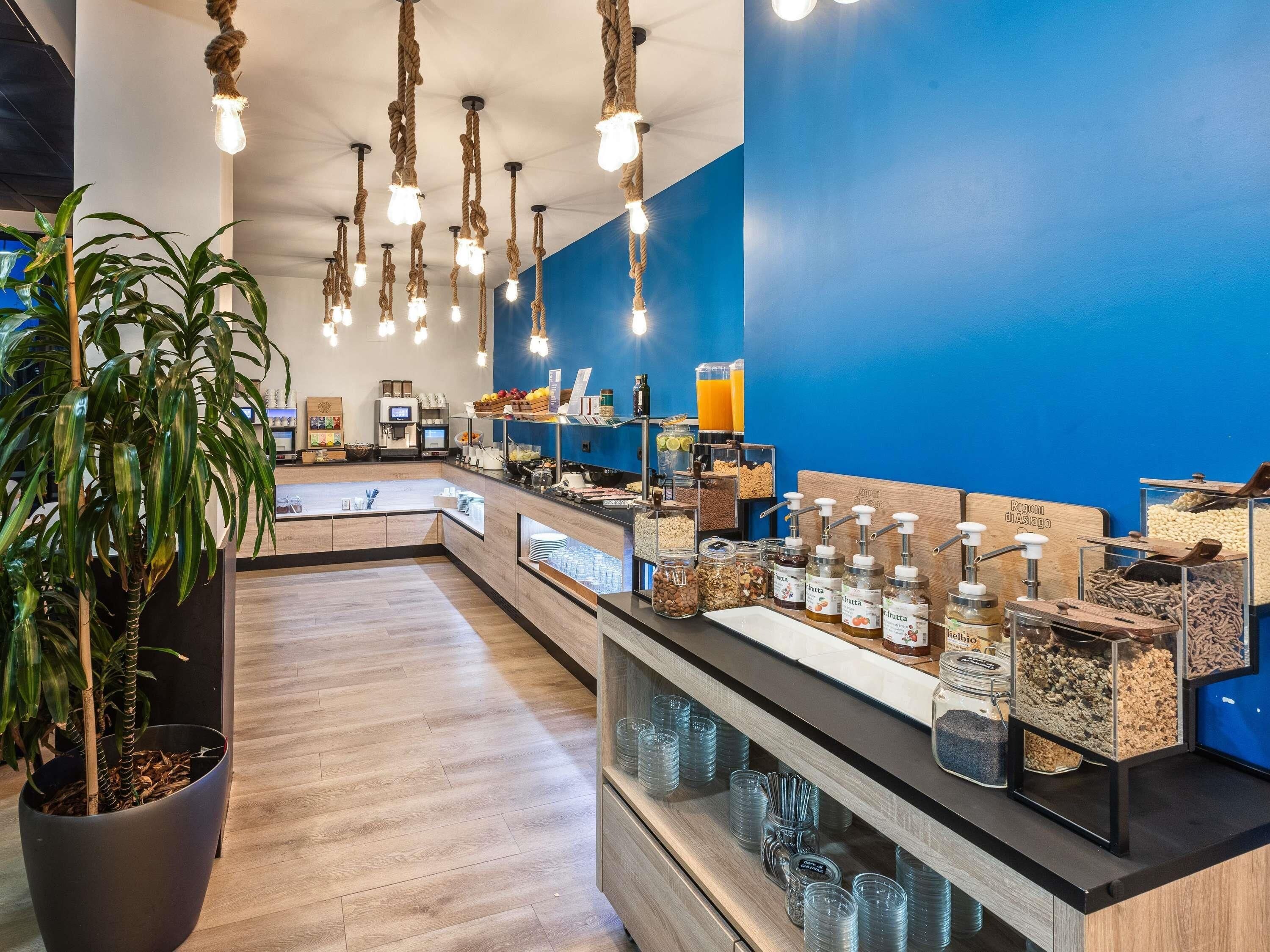 Um balcão de café da manhã moderno, com uma parede azul de destaque, luzes de corda penduradas e diversas opções para o café.