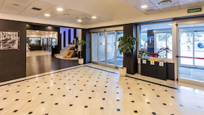 A lobby with a tiled floor, a reception desk, a large teddy bear, potted plants, and a security sign.