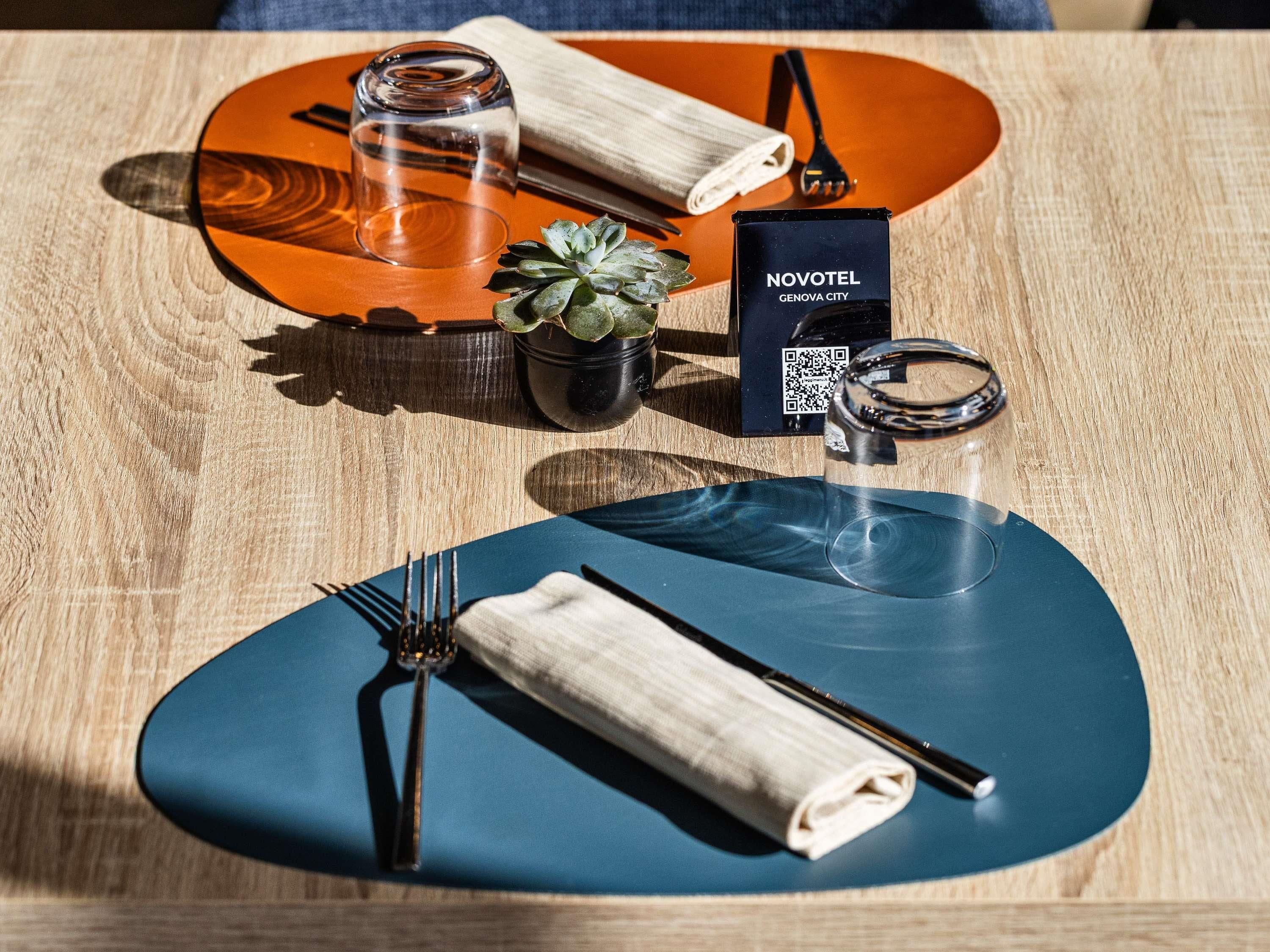 Une table avec un code QR, un verre, une serviette roulée, une fourchette, un couteau et une petite plante en pot.