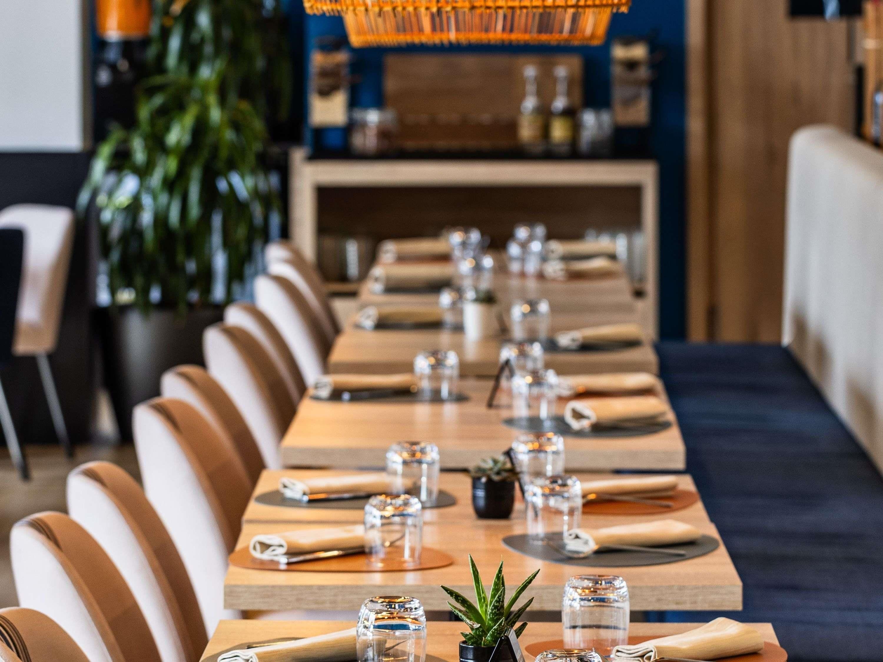 Una larga mesa de comedor con sillas, vasos y pequeñas macetas.