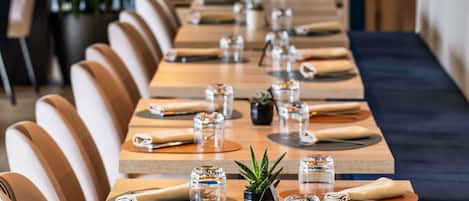 Una larga mesa de comedor con sillas, vasos y pequeñas macetas.