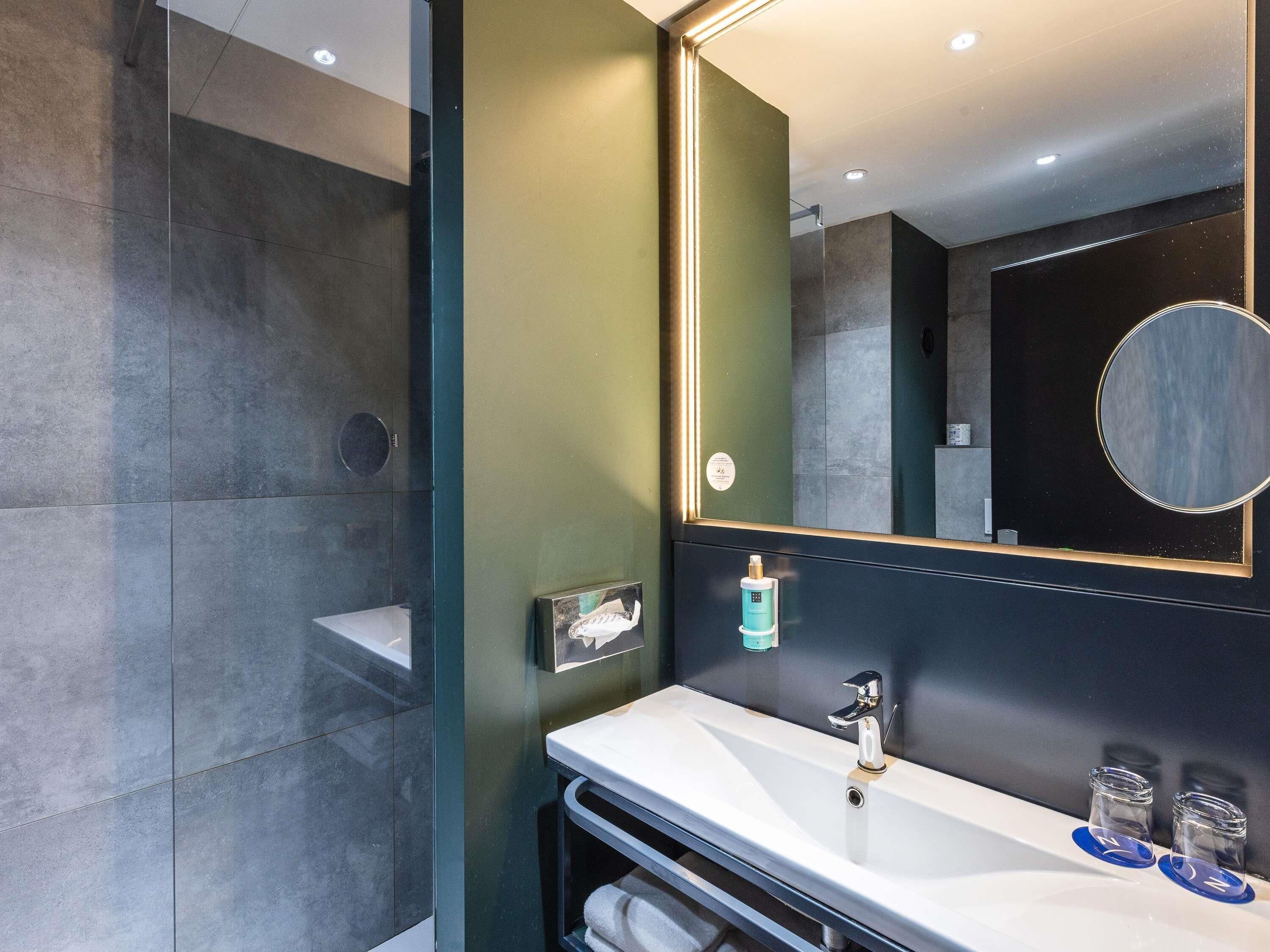 A modern bathroom with a glass shower enclosure, a large mirror, and a white sink with a faucet.