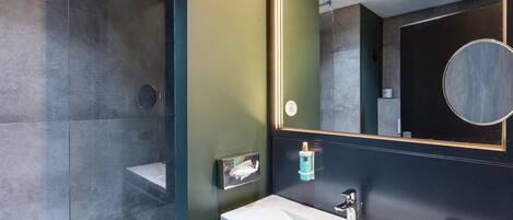A modern bathroom with a glass shower enclosure, a large mirror, and a white sink with a faucet.