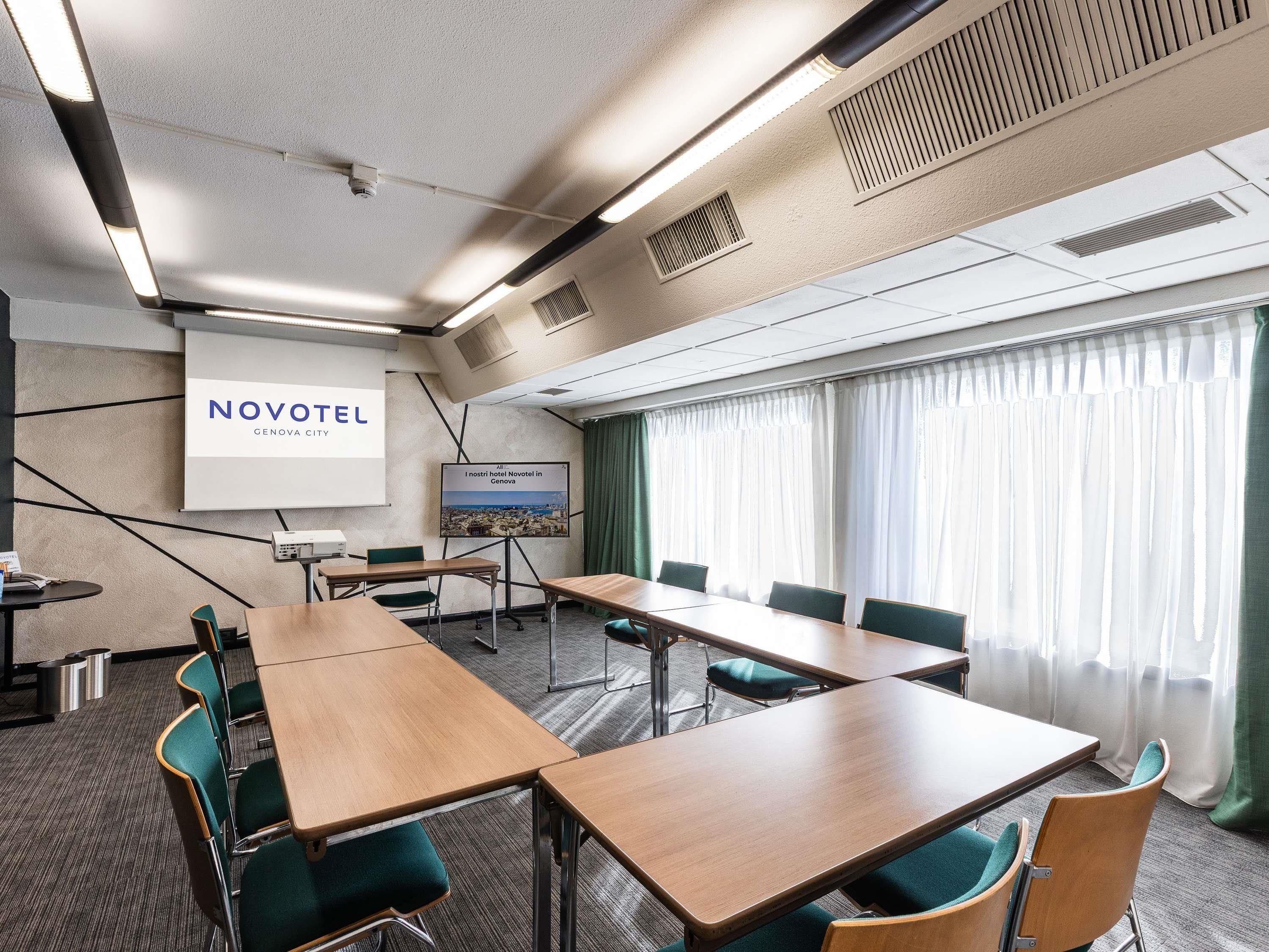 A hotel conference room with a large table, chairs, a projector screen, and a view of the city.
