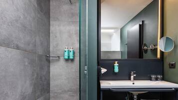 Ein modernes Badezimmer mit einer Glaskabine zur Dusche, einem großen Spiegel, einem Waschbecken und zwei Shampoo-Flaschen.