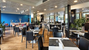 Un ristorante spazioso con soffitti alti, illuminazione moderna e diverse tipologie di posti a sedere.
