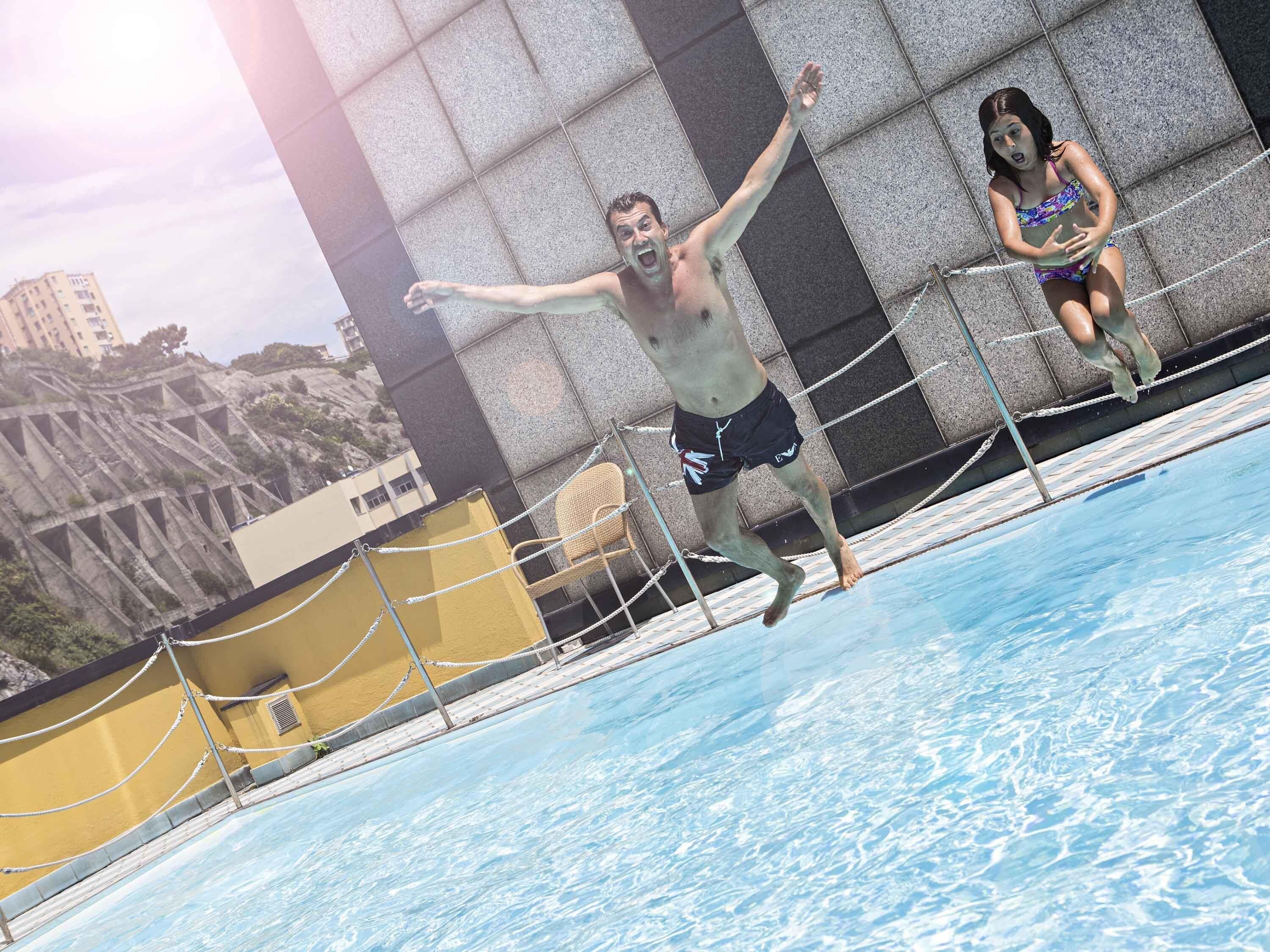 Ein Schwimmbecken mit Seilabsperrung, einer gelben Wand und einem Gebäude im Hintergrund mit markanter Architektur.
