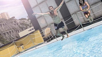 Ein Schwimmbecken mit Seilabsperrung, einer gelben Wand und einem Gebäude im Hintergrund mit markanter Architektur.