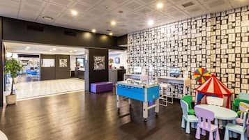 Eine moderne Lobby mit Holzboden, einer Rezeption, einem Kinderspielbereich mit bunten Zelten und einer Wand, die mit gerahmten Zeichnungen verziert ist.