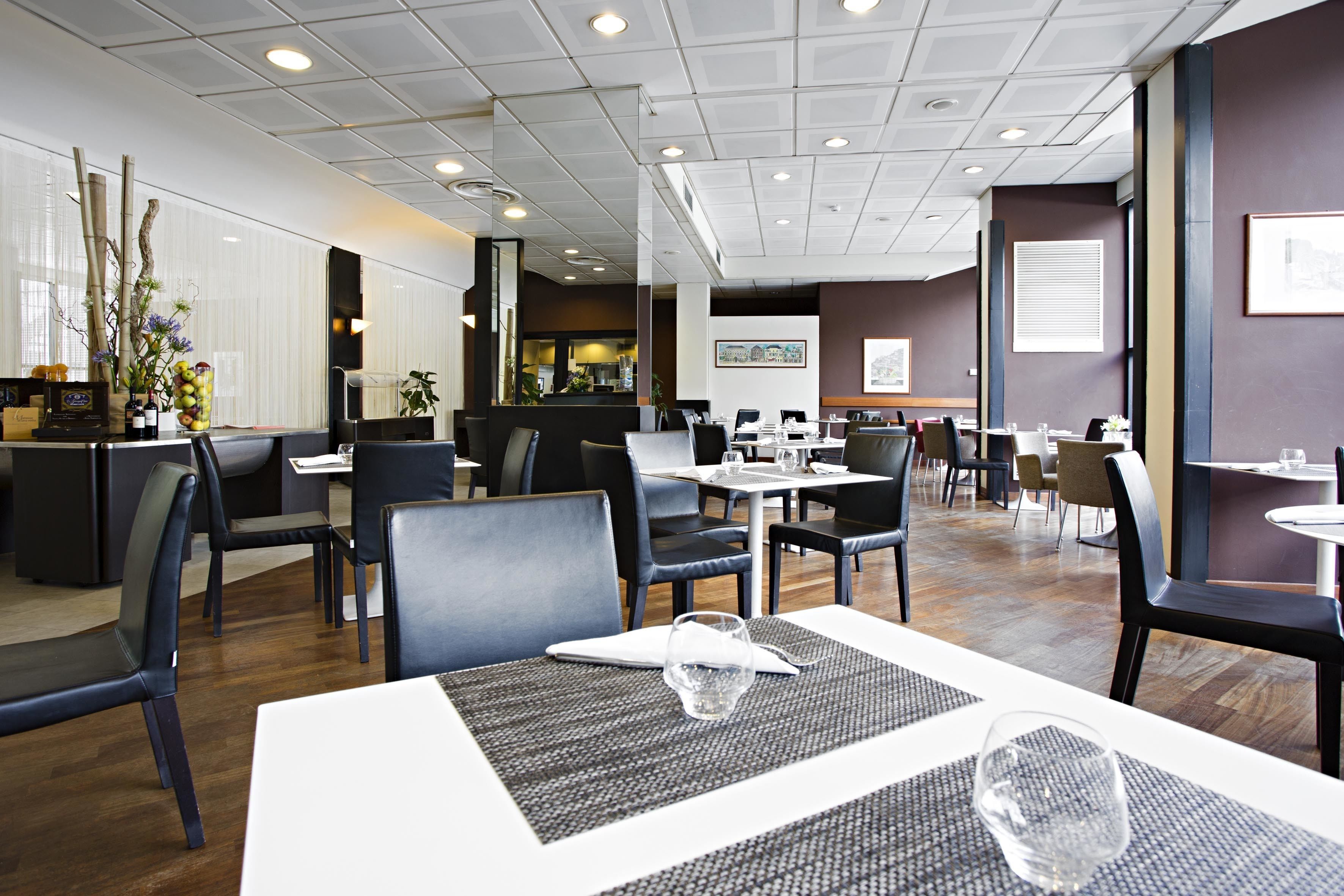 Un restaurante moderno con una distribución limpia y ordenada, con varias mesas y sillas, una zona de cocina visible y un interior bien iluminado.