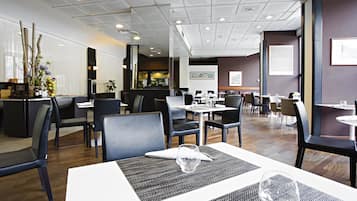 Un ristorante moderno con un'organizzazione pulita ed efficiente, con diversi tavoli e sedie, una cucina a vista e un ambiente ben illuminato.