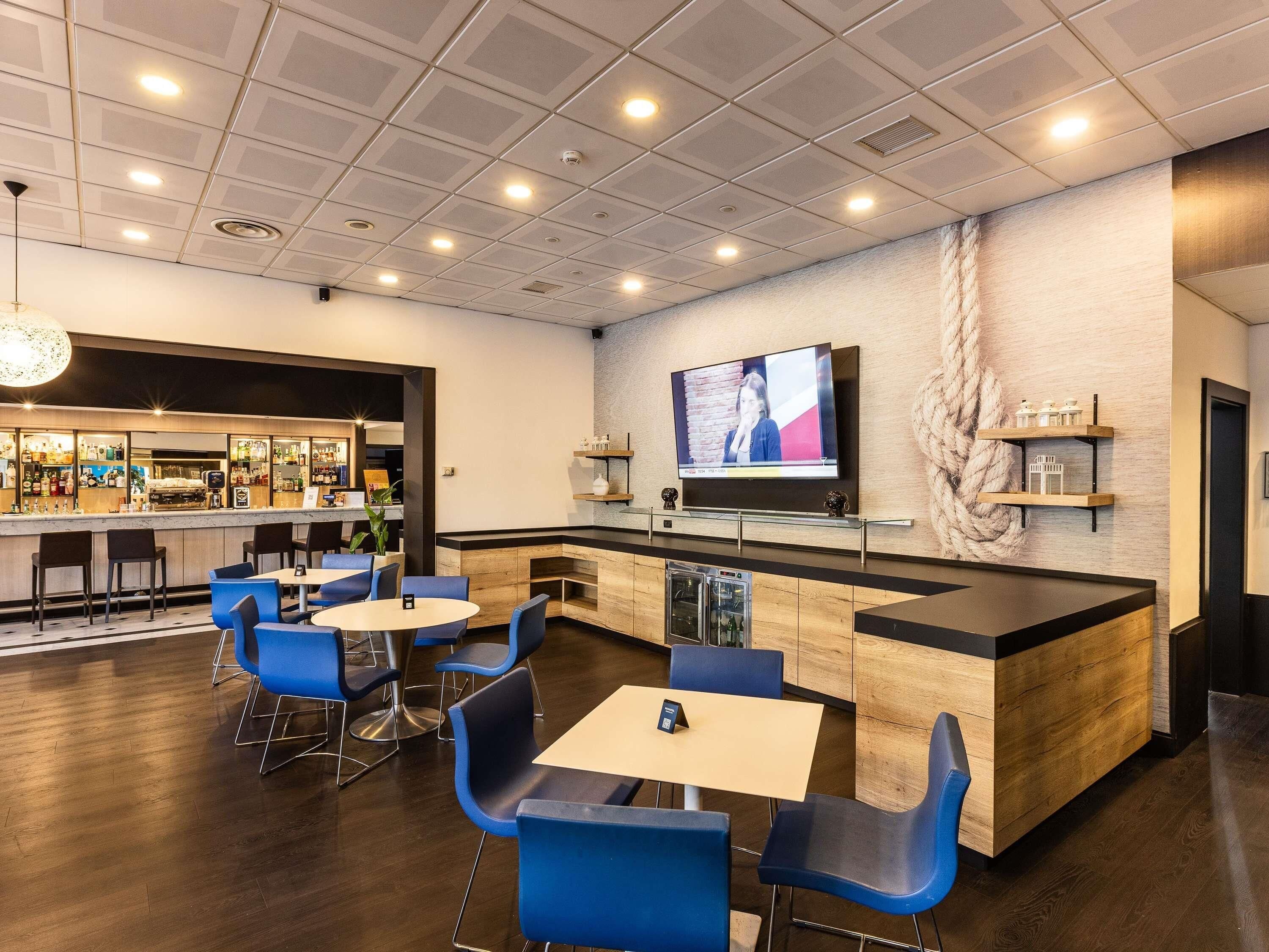 A modern bar area with a television screen, seating, and a bar counter.