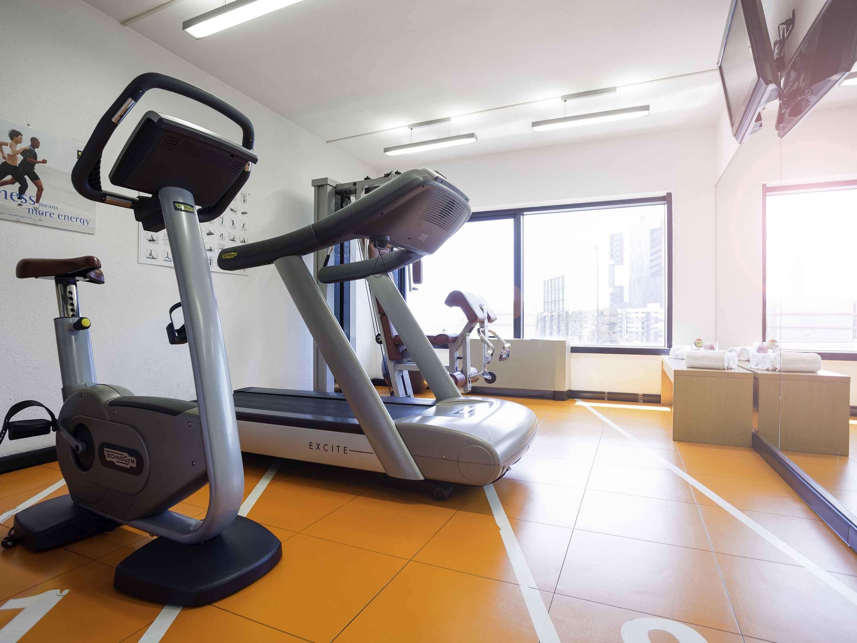 A gym with treadmills, exercise equipment, and a city view through large windows.