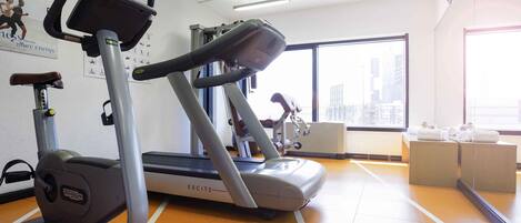 A gym with treadmills, exercise equipment, and a city view through large windows.
