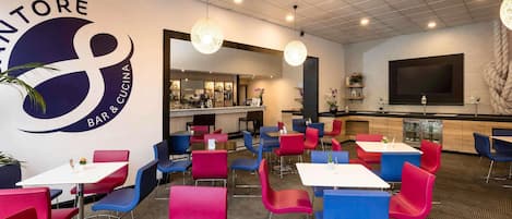 A restaurant with a bar and a kitchen area, featuring red and blue chairs and tables.