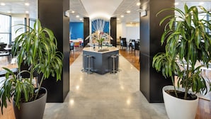 Una hall moderna con un'area bar centrale, grandi piante in vaso e una parete di colore blu.