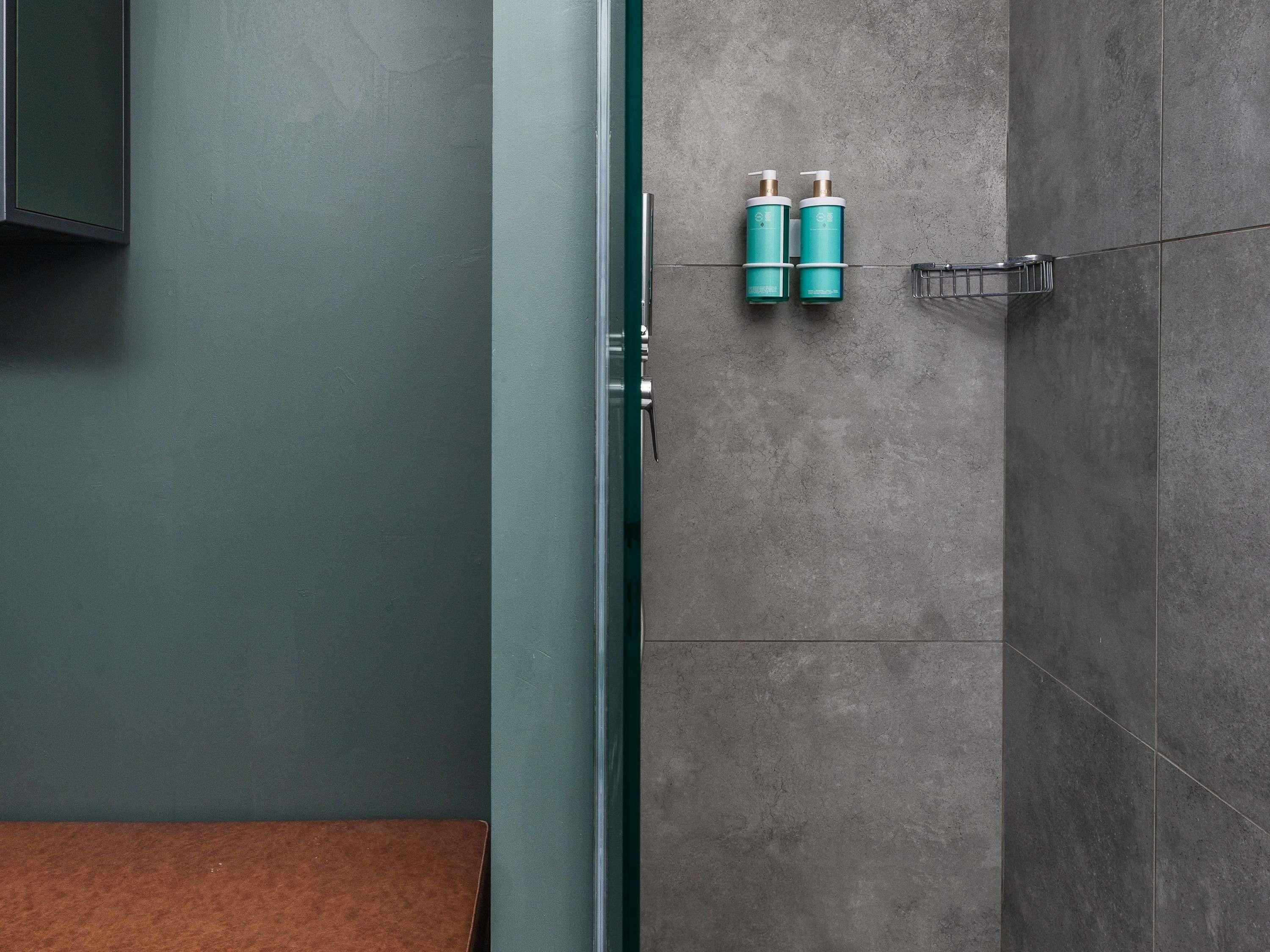 A bathroom with a grey wall, a wooden bench, and two teal bottles on a rack.