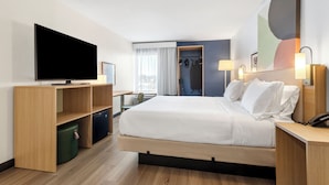 Une chambre d’hôtel moderne dotée d’un grand lit, d’un téléviseur à écran plat, de meubles en bois, d’un bureau et offrant une vue sur la ville.