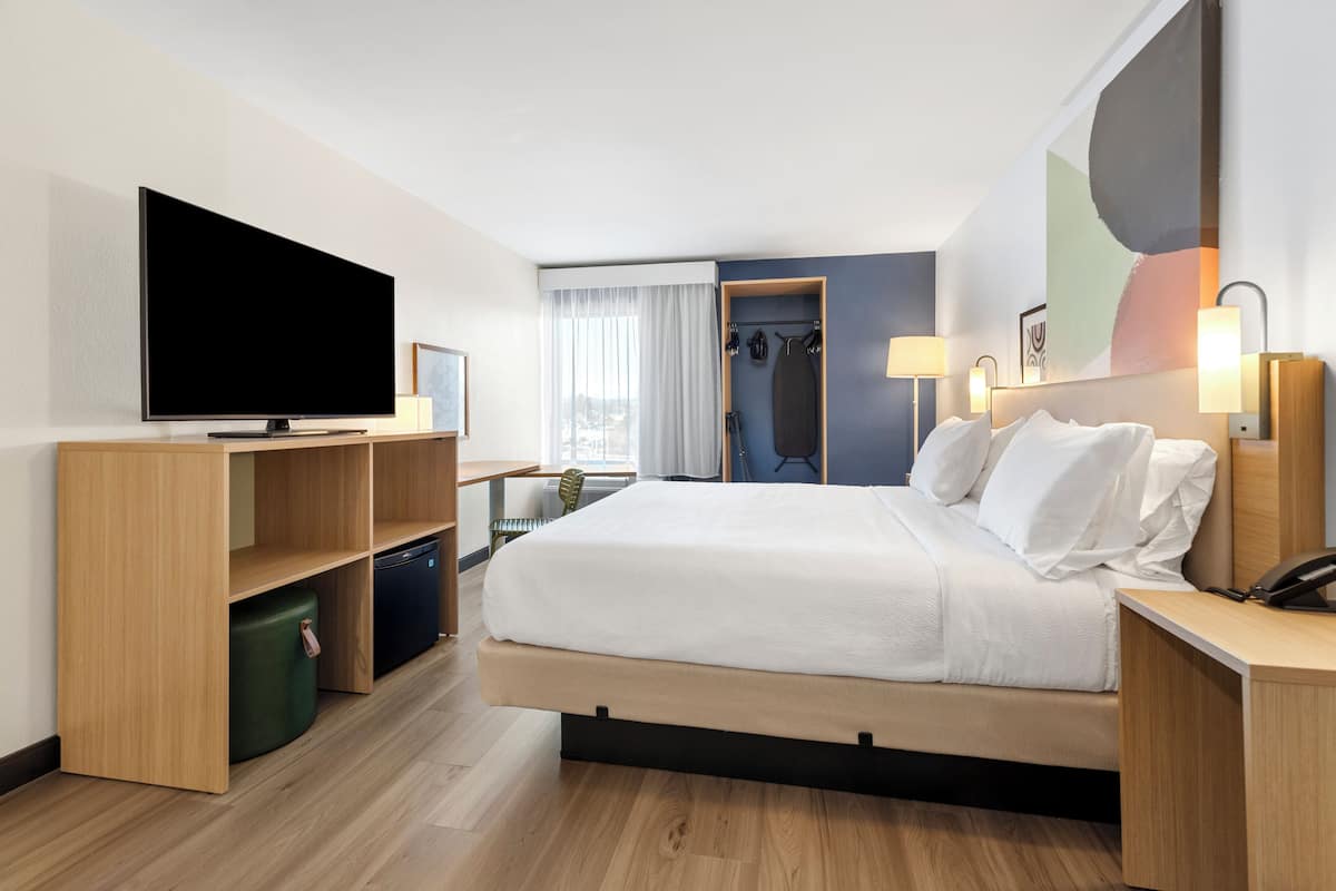 Ein modernes Hotelzimmer mit einem großen Bett, einem Flachbildfernseher, Holzmöbeln, einem Schreibtisch und Blick auf die Stadt.