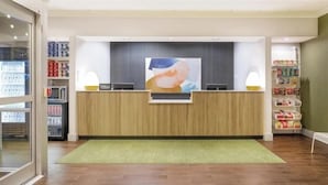 Un espace d’accueil avec un comptoir en bois, un grand tableau et des étagères remplies de produits.