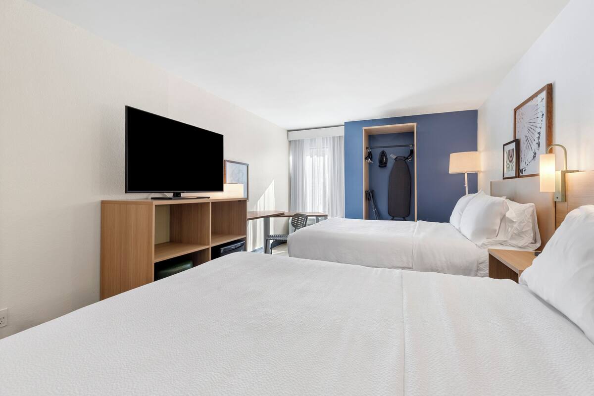 Ein Hotelzimmer mit zwei Betten, einem Fernseher, einem Schreibtisch und einem Kleiderschrank.