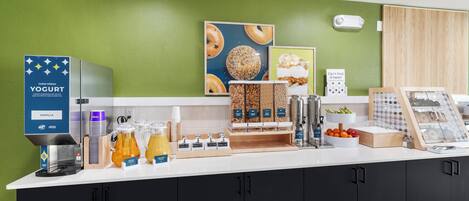 A breakfast bar with a yogurt dispenser, coffee maker, and various food items.