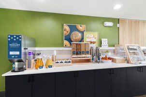 A breakfast bar with a yogurt dispenser, coffee maker, and various food items.