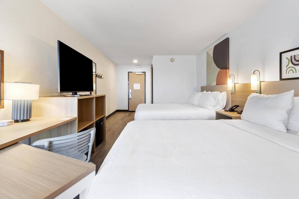 Ein Hotelzimmer mit zwei Betten, einem Schreibtisch, einem Fernseher und einem Sessel.