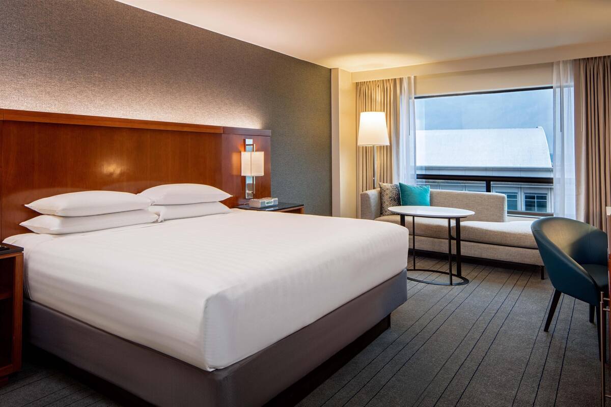 Habitación de hotel con una cama grande, un escritorio, una silla, una mesita y una ventana con cortinas.