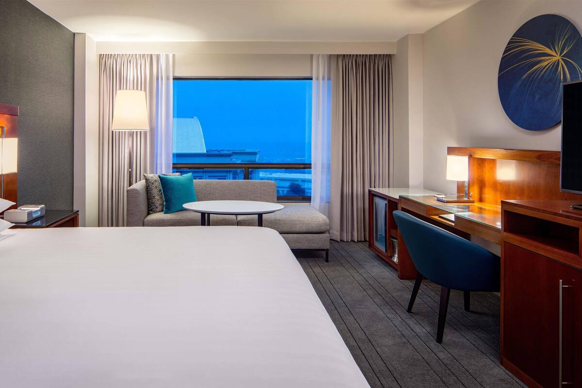 Habitación de hotel con cama, escritorio con silla, sofá, una mesita redonda y un ventanal con vistas.