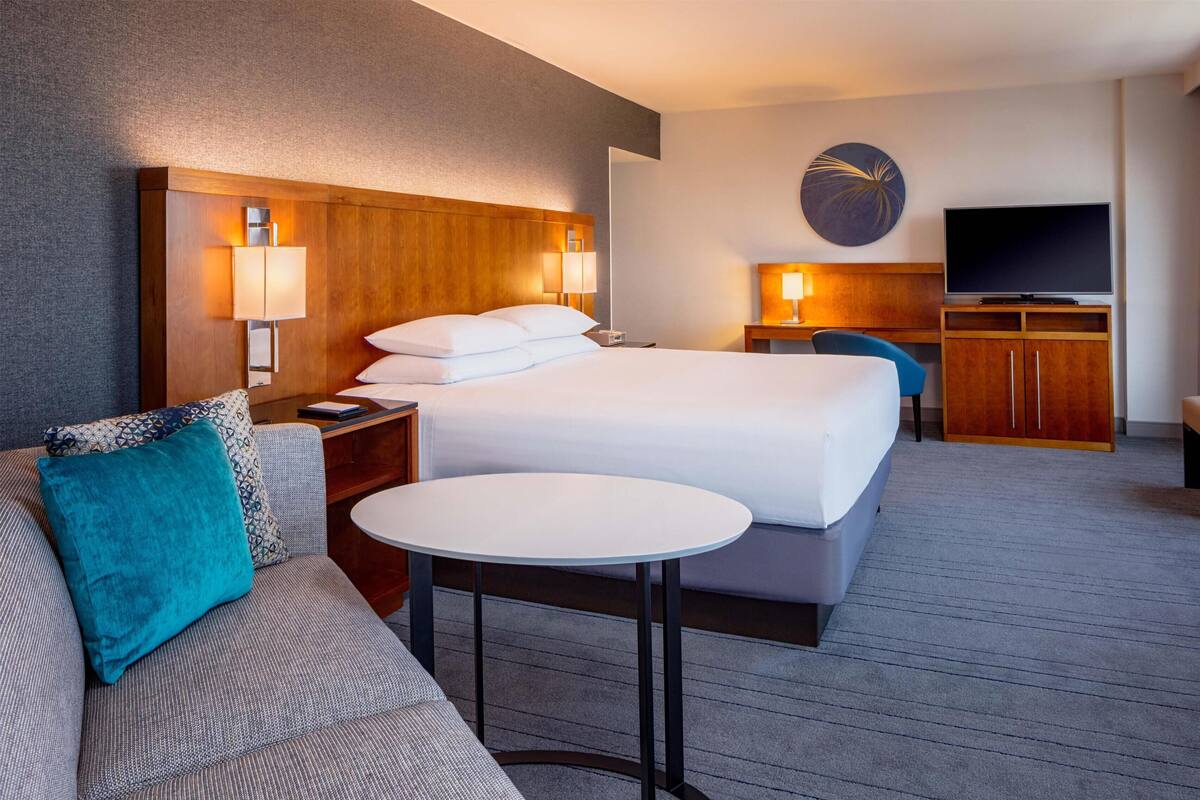 Una habitación de hotel con cama, sofá, una mesita, televisor y un reloj de pared.