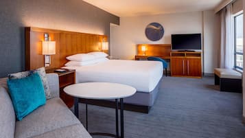 Una habitación de hotel con cama, sofá, una mesita, televisor y un reloj de pared.