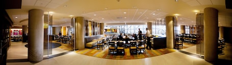 A spacious hotel lobby with multiple seating areas, a central bar, and a view of the lobby area in the background.