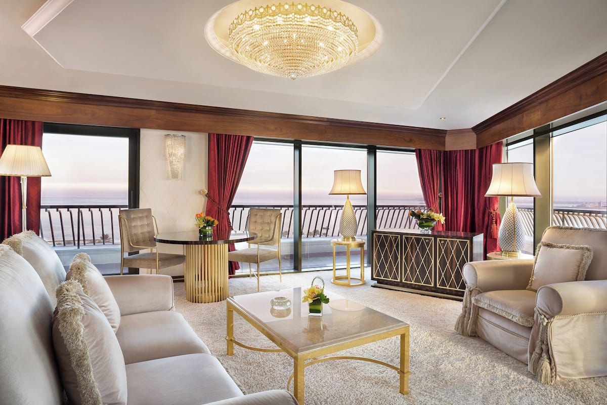 A spacious living room with a large chandelier, comfortable seating, and a view of the ocean.