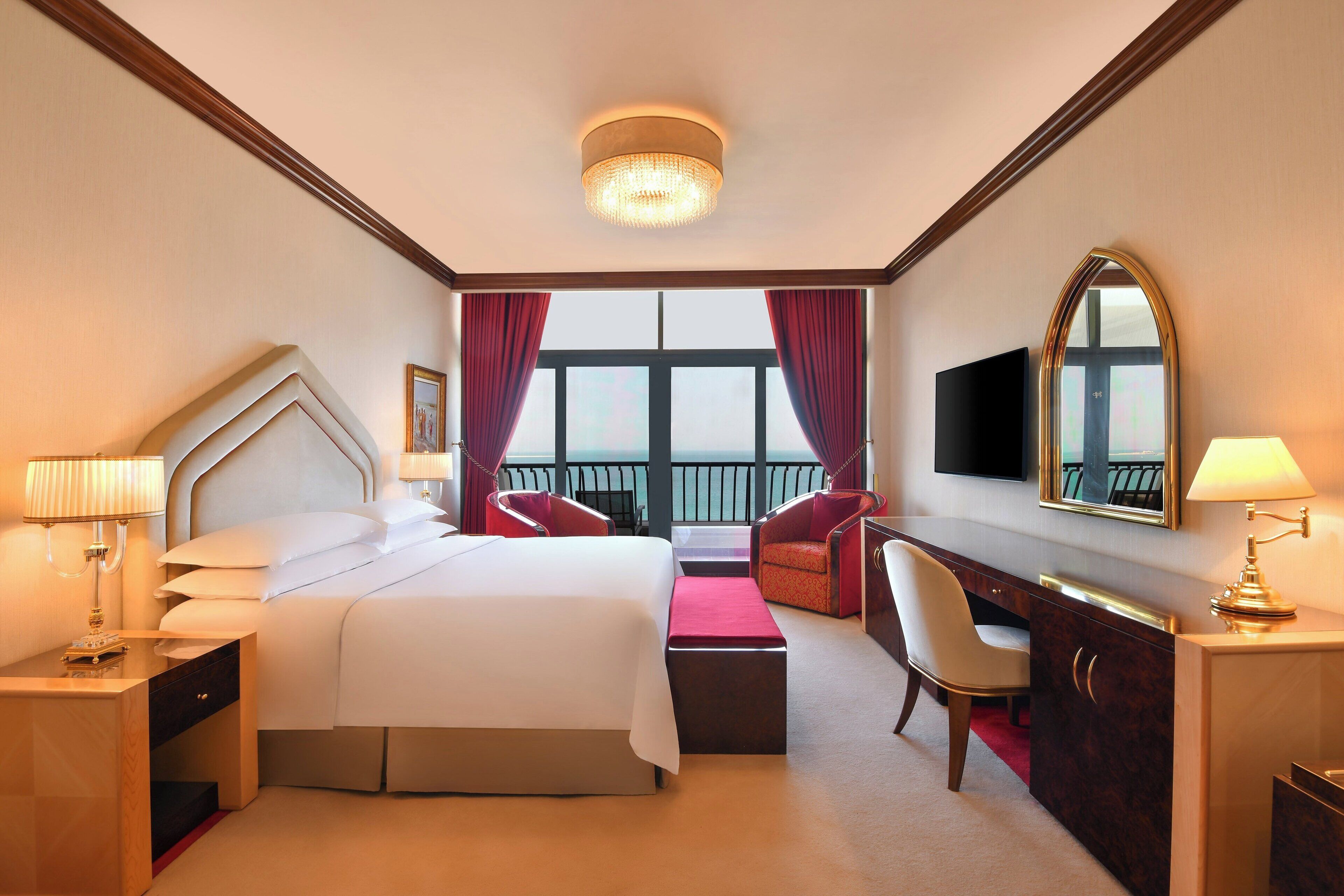 Habitación de hotel con una cama grande, un escritorio, una silla, televisión y vistas al balcón.