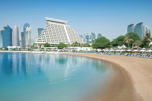 Un hotel frente a la playa con diseño moderno, piscina y zona de playa con tumbonas.