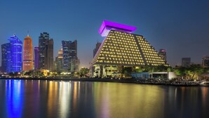 Un hotel moderno con una estructura piramidal única, situado cerca de una masa de agua que refleja el paisaje urbano circundante.