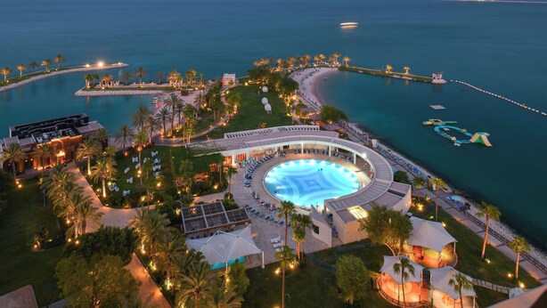 Un resort con una piscina grande, zona de playa y palmeras.