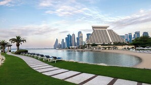 Un hotel frente al agua con un diseño arquitectónico moderno, un área de piscina con sillones de descanso y vistas al horizonte de la ciudad.