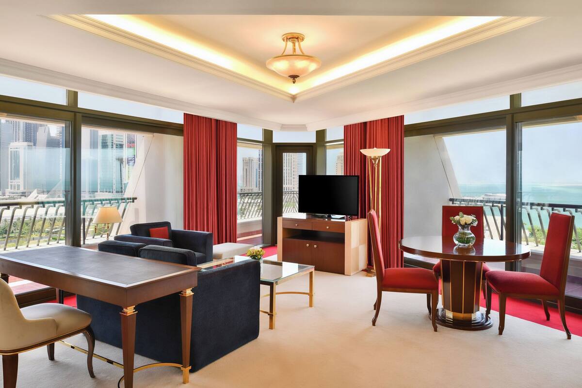 A hotel room with a large window, a flat-screen TV, a dining table, and a sofa.