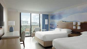 Une chambre d’hôtel avec deux lits, un bureau, une chaise, une télévision et un balcon offrant une vue sur la ville.